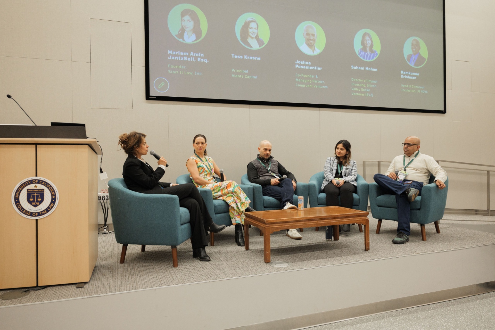 Full Capital Day investor panel seated on the UC Law SF stage beneath the speaker line-up slide