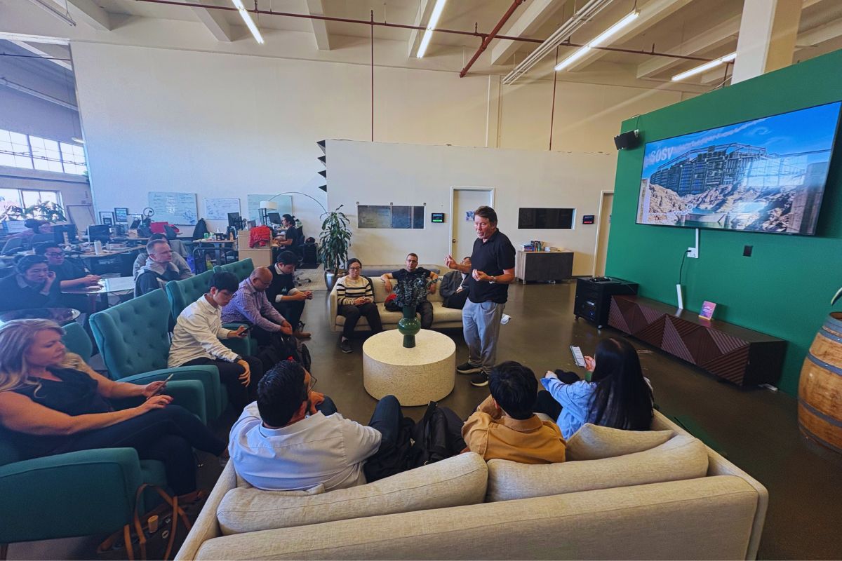 Wide overview of the SOSV office lounge during Frontiers Day with founders and investors seated around the host and the SOSV branded screen
