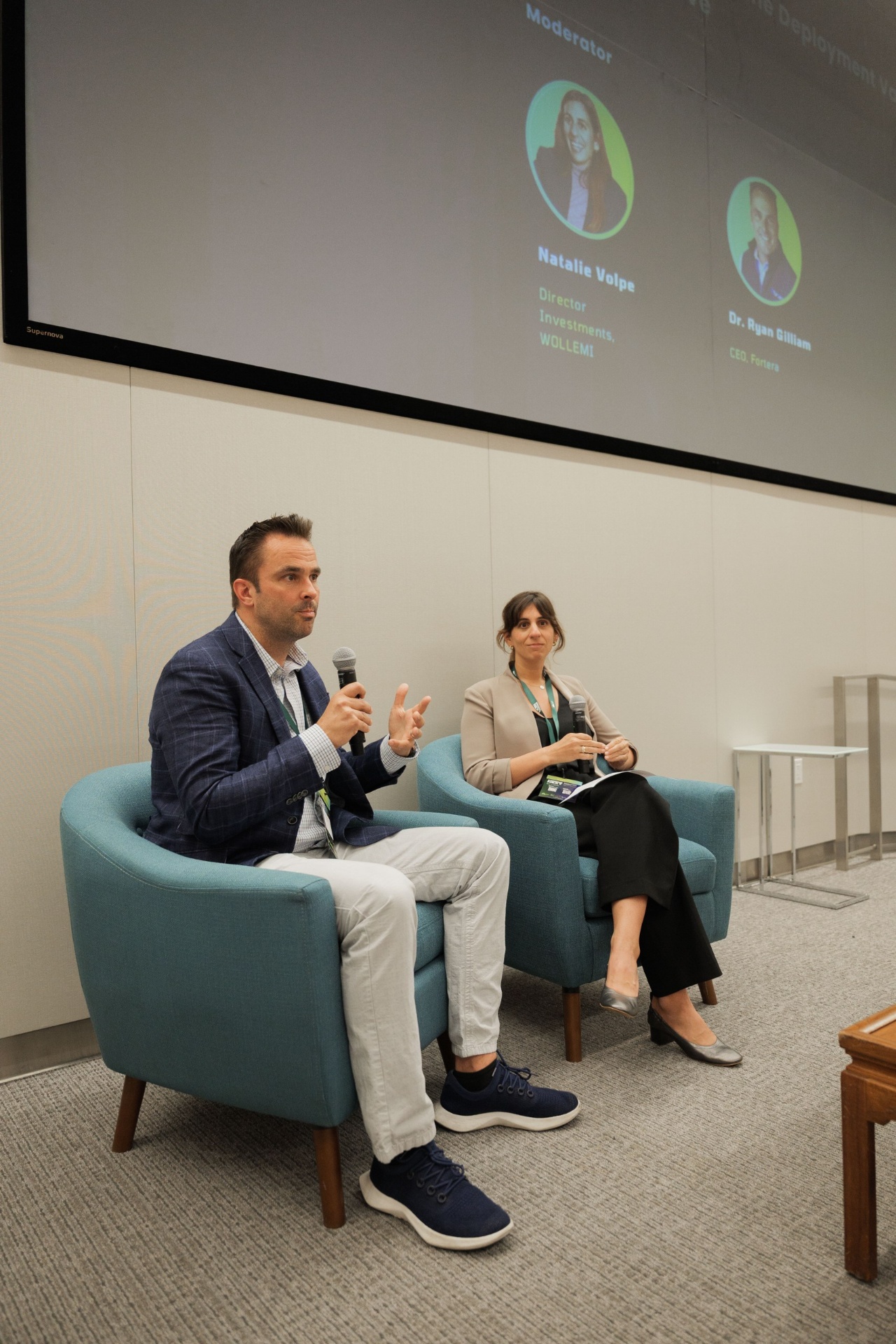 Capital Day fireside chat wide shot — Dr. Ryan Gilliam, CEO of Fortera, in conversation with moderator Natalie Volpe of WOLLEMI beneath the speaker line-up slide at UC Law SF