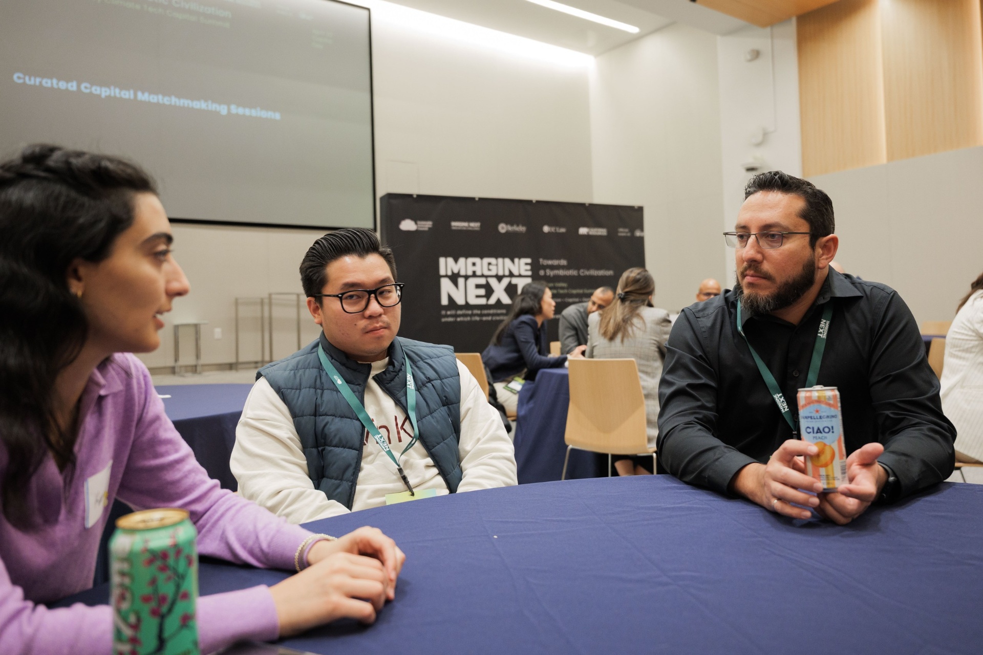 Three delegates in animated conversation during the Capital Day Curated Capital Matchmaking Sessions at UC Law SF beneath the Imagine Next banner