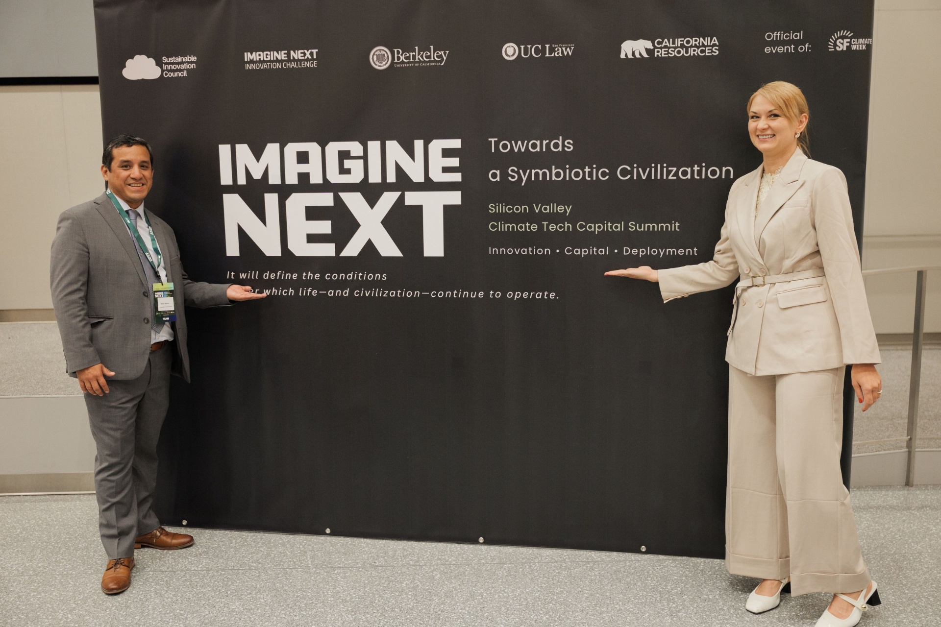 Imagine Next 'Towards a Symbiotic Civilization' Silicon Valley Climate Tech Capital Summit backdrop at UC Law SF with two team members posing alongside the Sustainable Innovation Council, Imagine Next Innovation Challenge, UC Berkeley, UC Law, California Resources and SF Climate Week sponsor logos