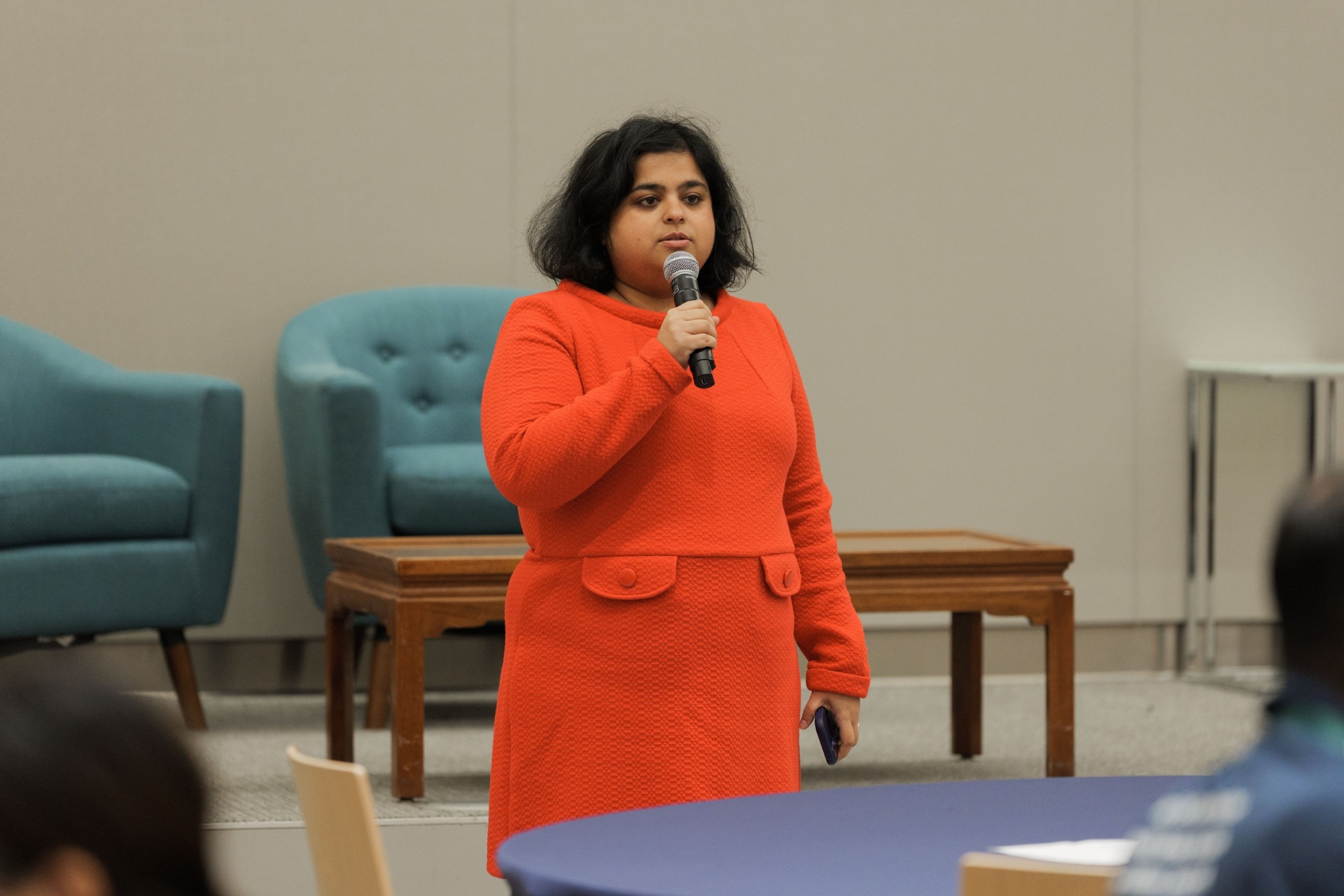 Delegate in an orange dress speaking with mic during a Capital Day session at UC Law SF