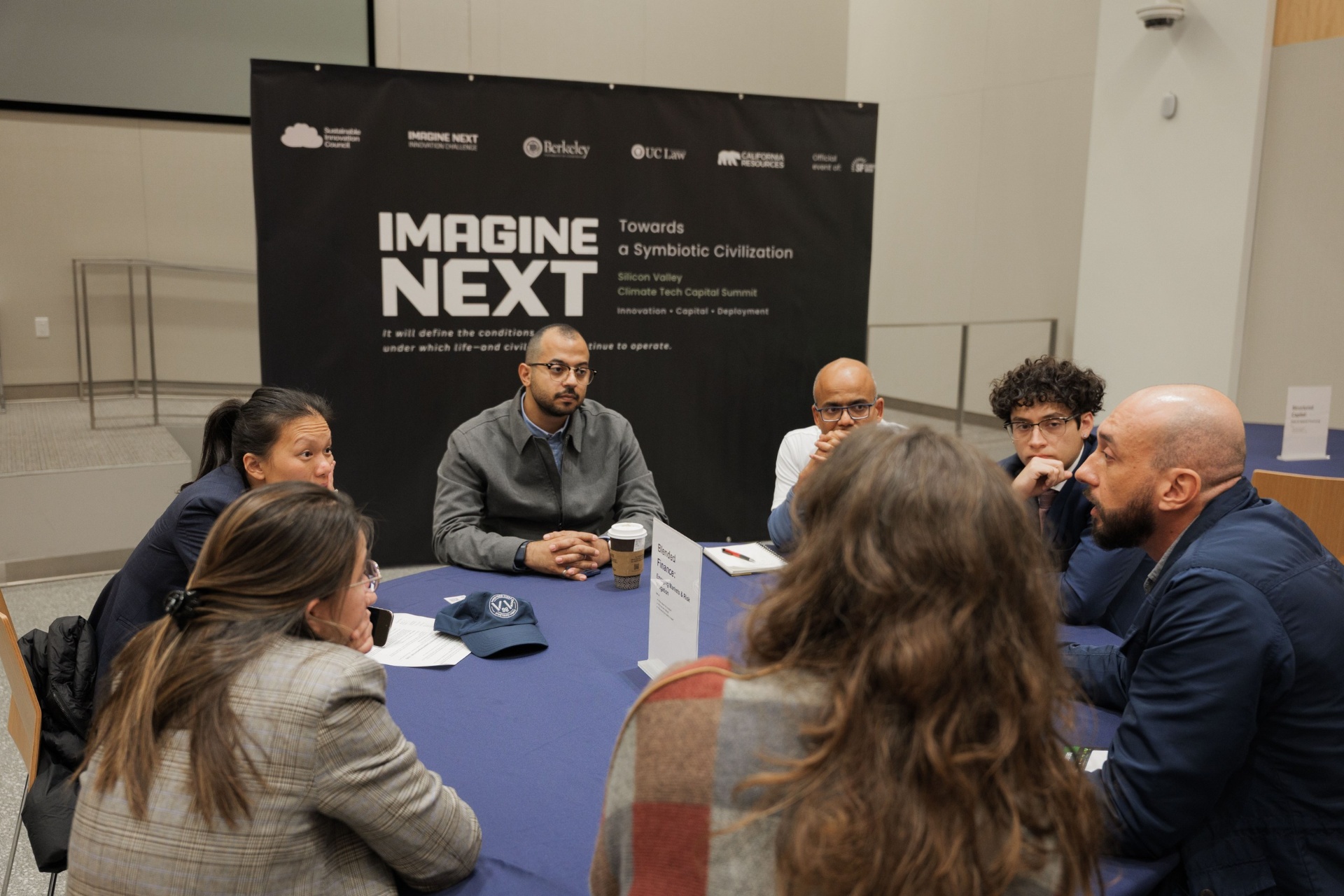 Capital Day Curated Capital Matchmaking Session — 'Blended Finance: Emerging Markets & Risk Mitigation' table with founders and investors in conversation beneath the Imagine Next banner at UC Law SF